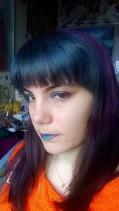 [Justine CM] Photo de moi où l'on voir ma frange turquoise et le reste de mes cheveux violets. Fard à paupières, crayon à paupières et rouge à lèvres avec les mêmes teintes. Pull orange.