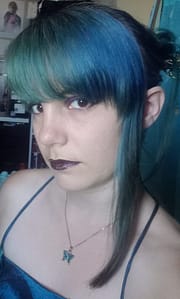 [Justine CM] Portrait de moi avec mes cheveux bleus-verts (turquoise), attachés en chignon et retenus par un pic à cheveux. Frange et une mèche de cheveux à gauche encadrent mon visage. Fard à paupières et rouge à lèvres violets. Pendentif en forme de papillon bleu-vert.
