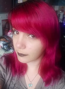 [Justine CM] Photo de moi avec les cheveux couleur rouge anglais. Je porte un rouge à lèvres noir, du crayon à paupières noir et un fard à paupières brun. Je porte un haut marron clair et mon pendentif papillon aux ailes turquoises.