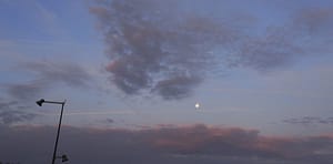 [Justine CM] Ciel gris, nuageux, aux nuages parcourus d'un rose léger, et la lune visible même en plein jour. Poteau électrique à gauche. Prise à la Gare TGV de Meroux-Moval.
