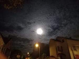 [Justine CM] Ciel noir et nuageux, où l'on voit la pleine lune. Lampadaire diffusant une lumière jaune.