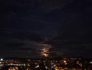 Photo d'un ciel nuageux de nuit, où la Lune joue à cache-cache, surplombant la ville de Belfort.